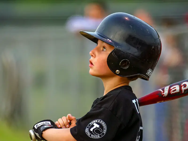 A young hitter in a helmet, bat on the shoulder, waiting on a pitch.